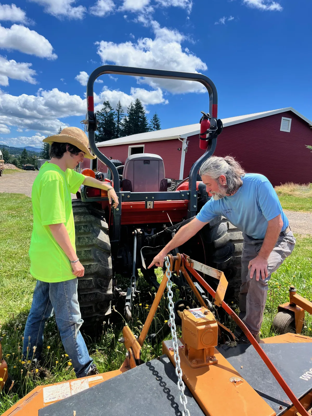 Farmer John showing an employee how to hook up a tractor