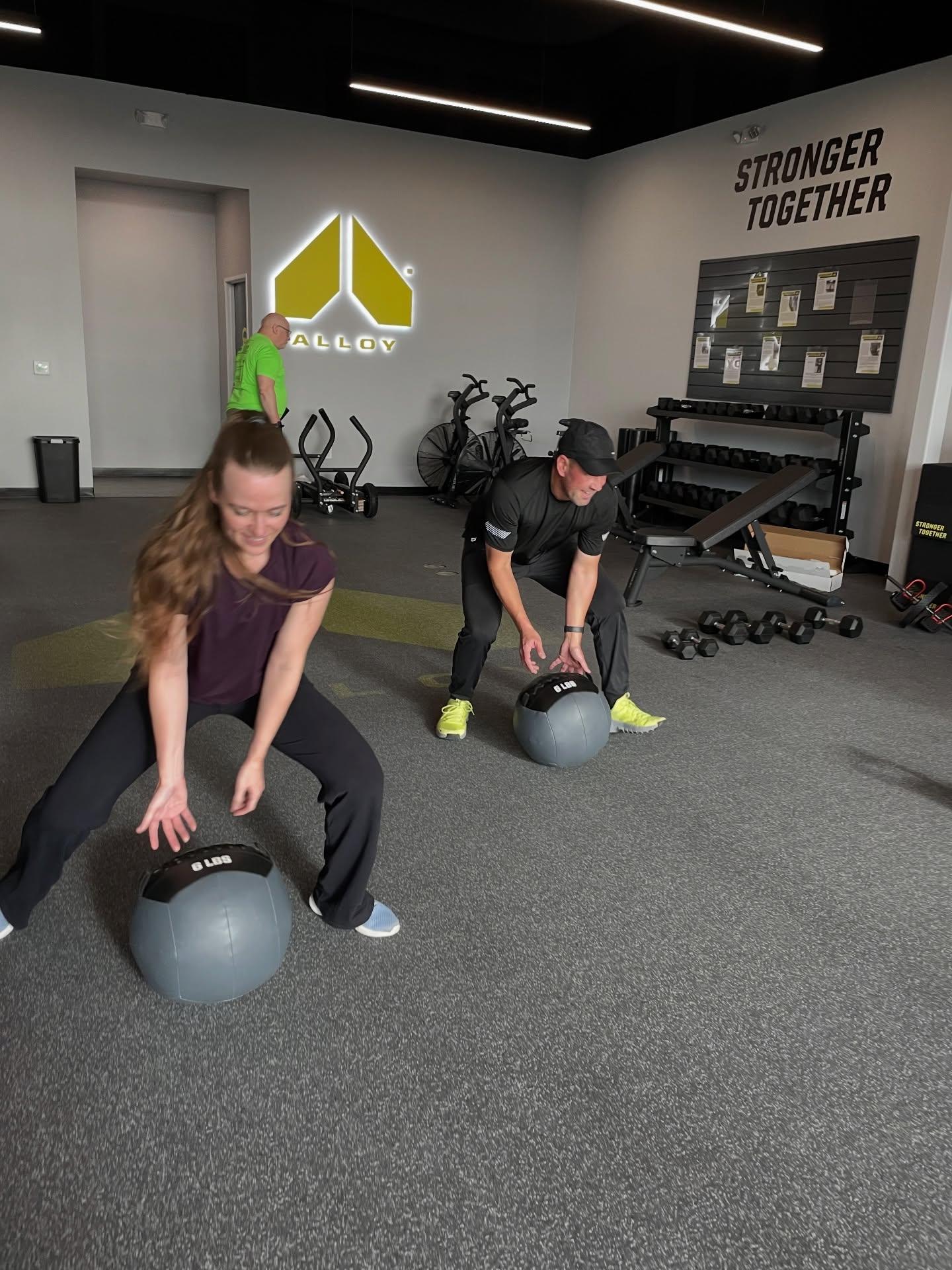 Two clients participated in a functional strength training session using medicine balls, guided by an Alloy personal trainer in a group fitness class at Alloy Personal Training Cedar Hills Crossing, Beaverton. The environment promotes strength training, mobility, and personalized coaching for all fitness levels.