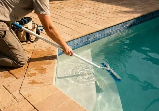 Technician kneeling on a paver deck brushing the pool steps during a monthly service visit