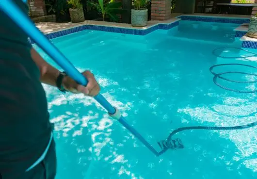 Pool technician vacuuming the floor of a backyard pool on a weekly service route in Fort Pierce