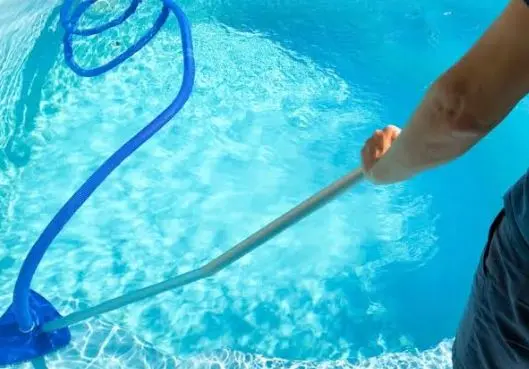 Technician vacuuming a clear blue pool with a telescopic pole and hose during pool maintenance in Fort Pierce