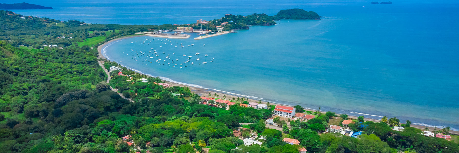 A friendly bilingual team member at a modern reception desk with a Costa Rican flag, tropical plants, and ocean view.