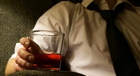 Man passed out on a couch holding a glass of whiskey, illustrating the consequences of excessive drinking.