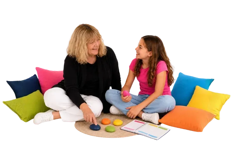 Lozz Kennedy sitting with a girl among colourful cushions, using grounding stones and a personalised calm-plan notebook.