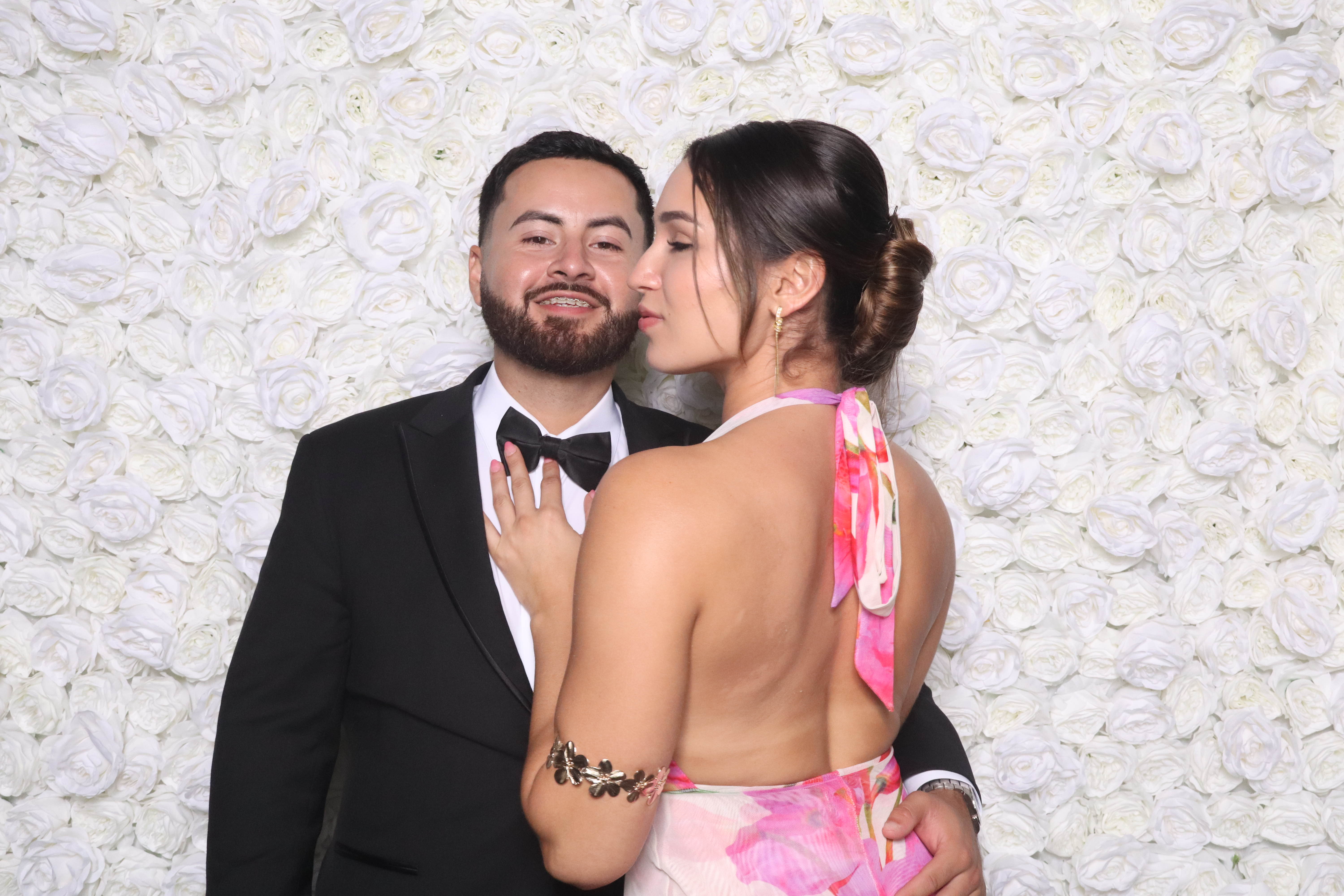 Elegant couple holding a keepsake print, smiling in front of a floral arch, with natural daylight streaming through large windows, creating a dreamy, romantic scene.