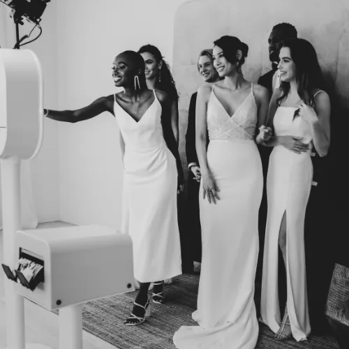 A group of wedding guests posing with playful props in a Miami ballroom, soft pink uplighting, and a shimmering sequin backdrop, capturing a fun, lively moment.