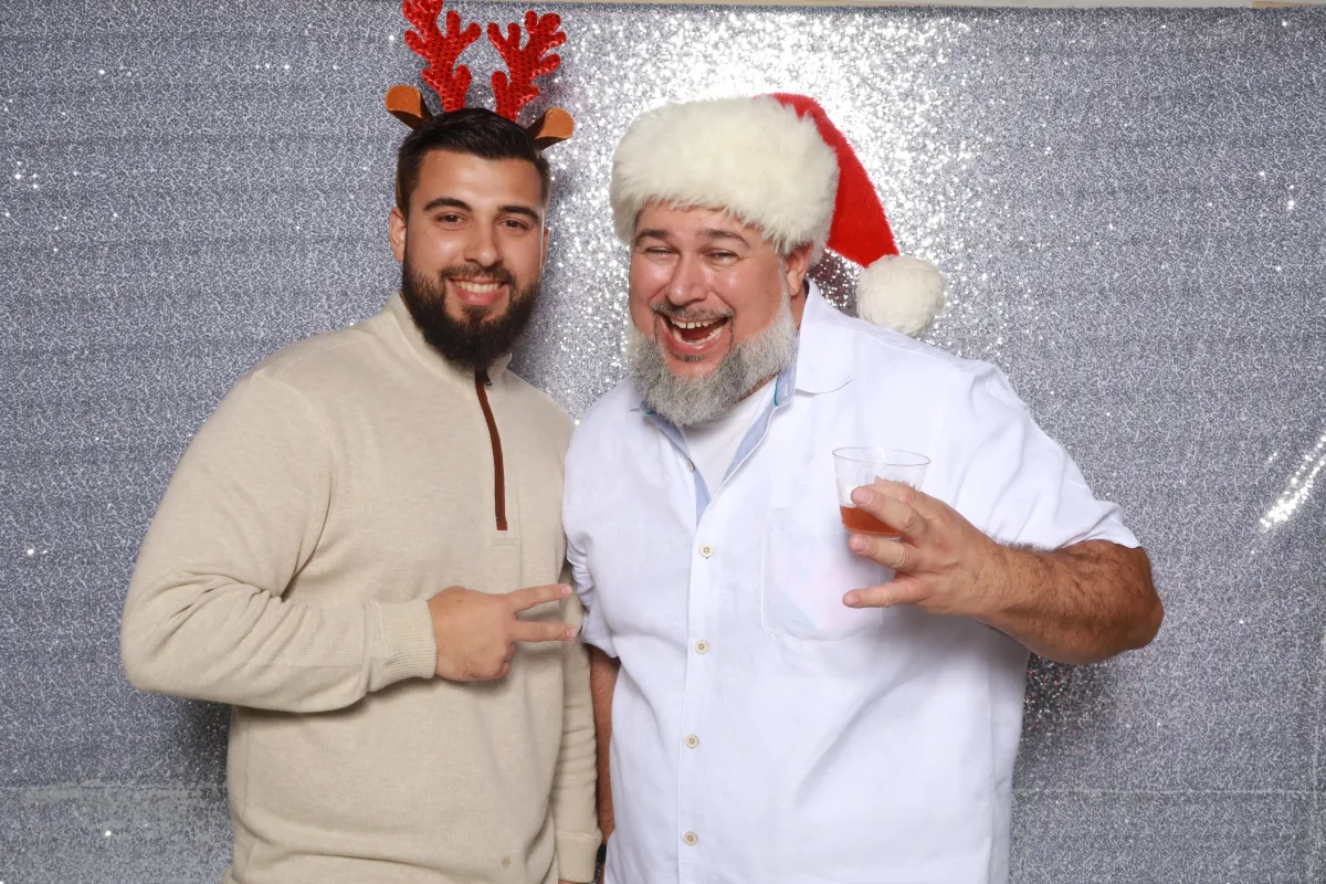 Two friends laughing inside the booth mid-pose, candid joy, teal backlight and pink rim lighting, natural skin tones and shallow depth-of-field capturing spontaneous energy at a nighttime rooftop party.