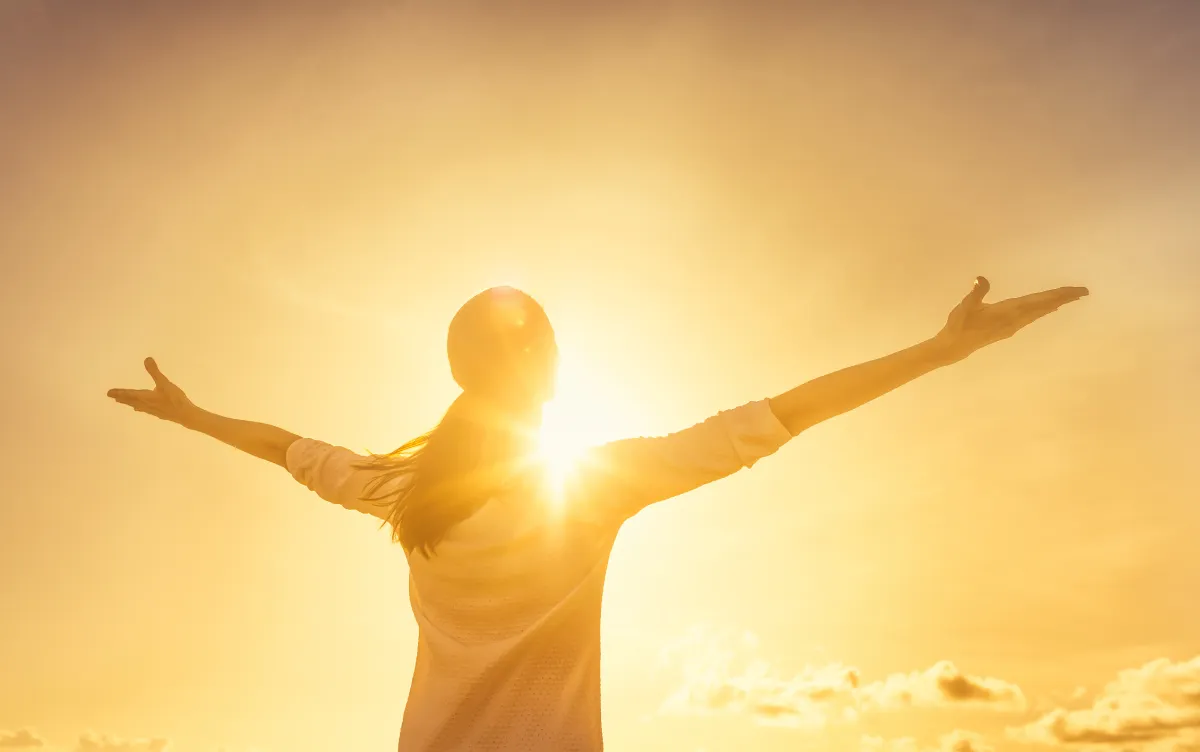 woman with arms raised at sunrise