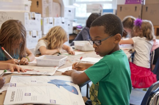 boy in green sweater writing on white paper