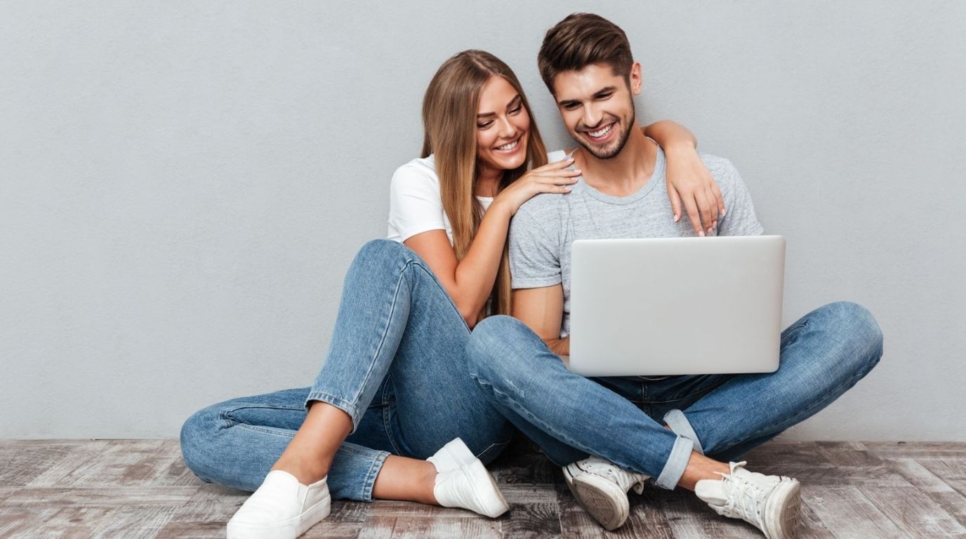 junges, verliebtes Paar sitzt am Boden und schaut in den Laptop