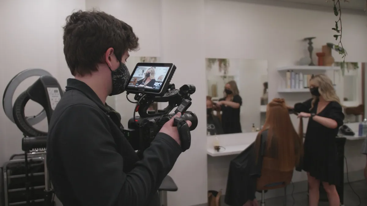 Camera operator framing a hairdressing demonstration in a salon
