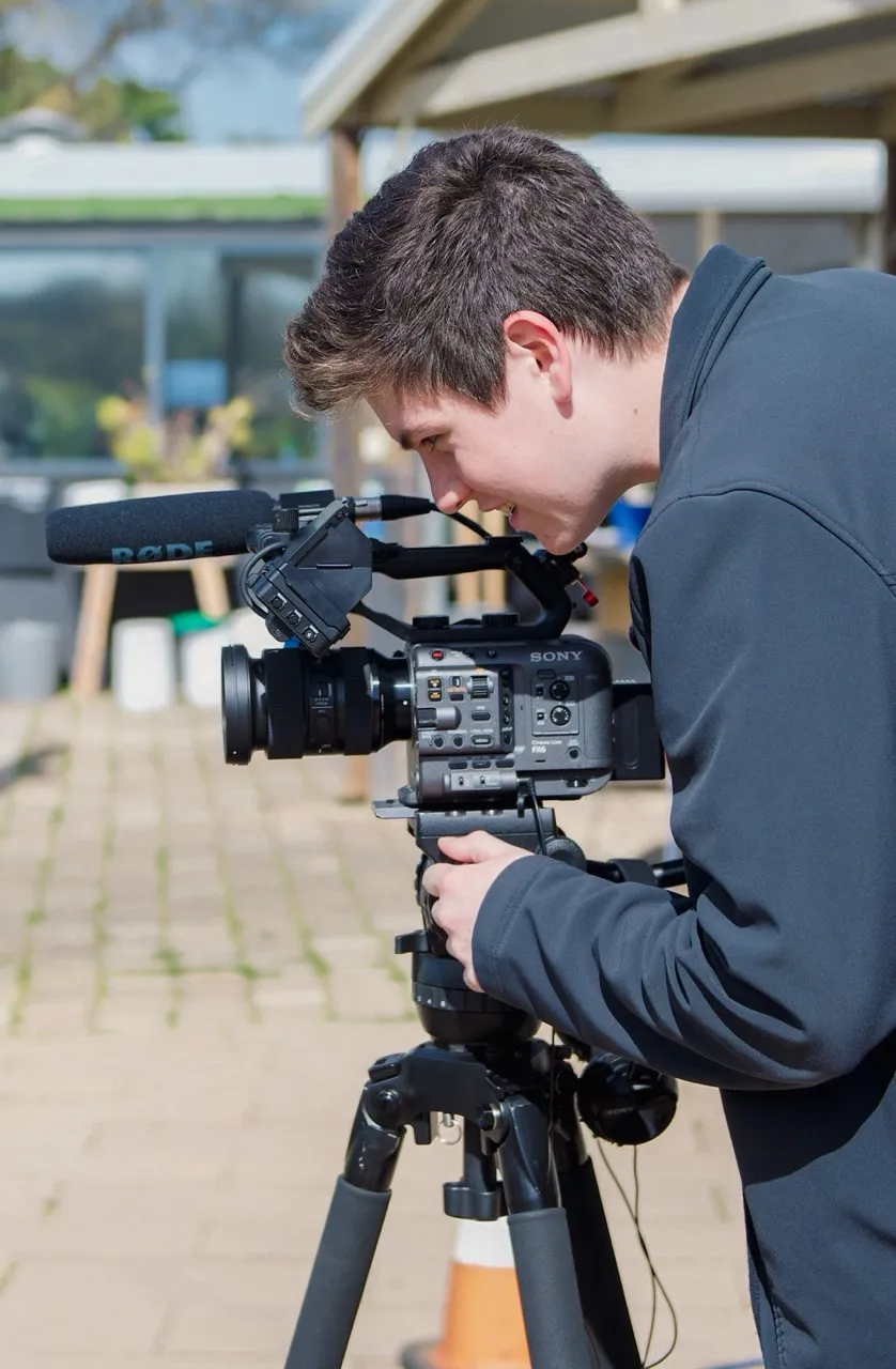 Henry looking through a cinema camera on a tripod at an outdoor shoot