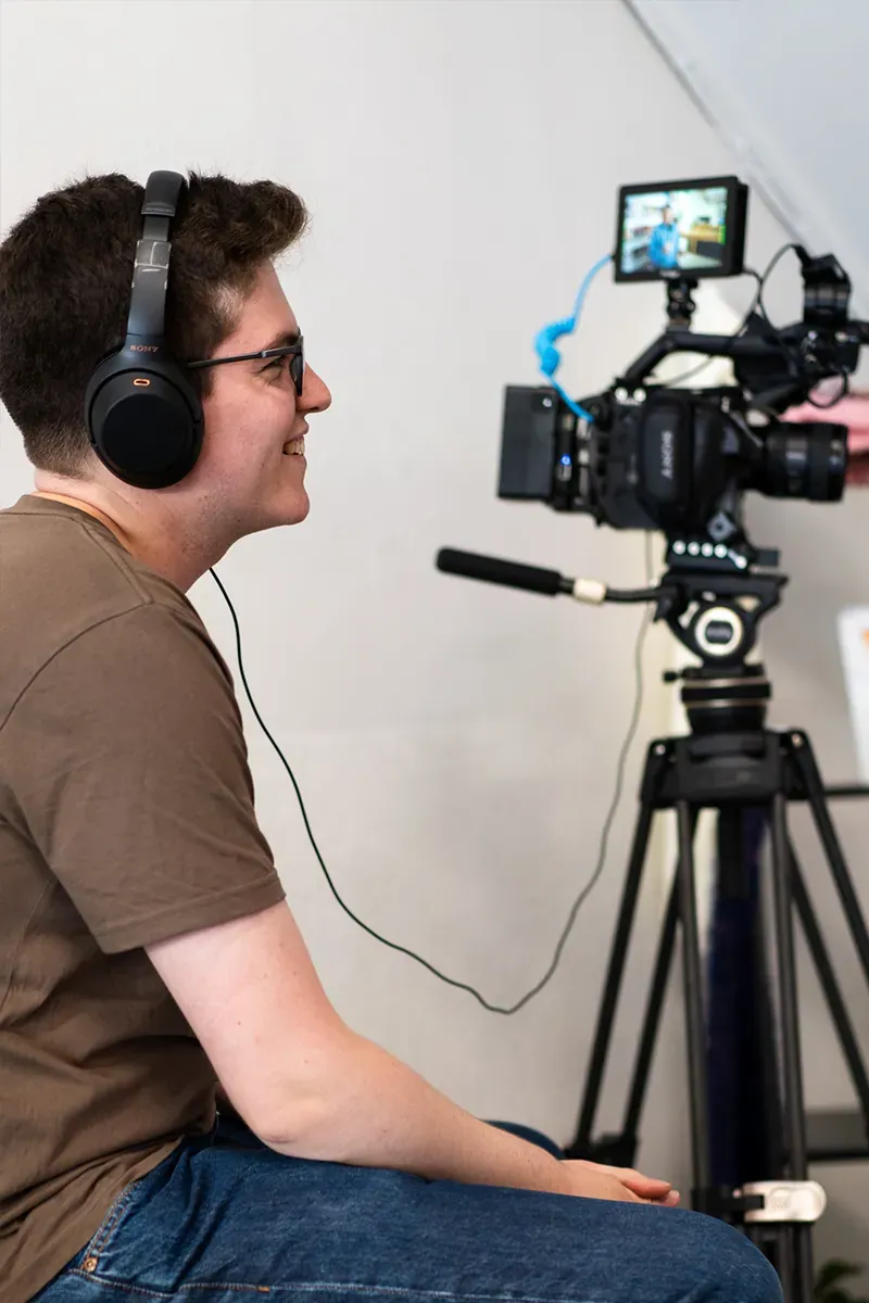 Henry in headphones watching the monitor beside a cinema camera on set
