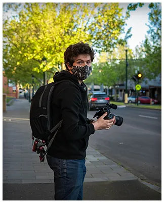 Henry shooting handheld on a suburban street, camera bag on his back