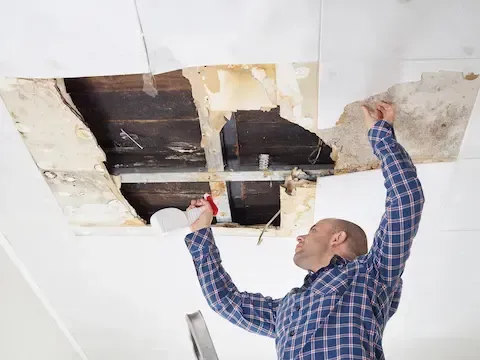 Worker inspecting water-damaged ceiling for mold – Huntsville Mold Removal Pros.