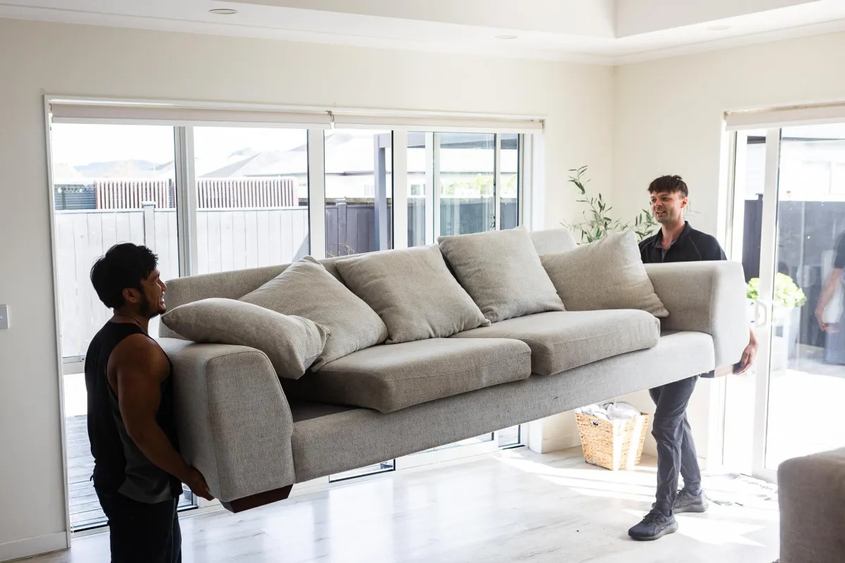 Two movers carrying a refrigerator down stairs, demonstrating professional furniture moving services in Auckland.