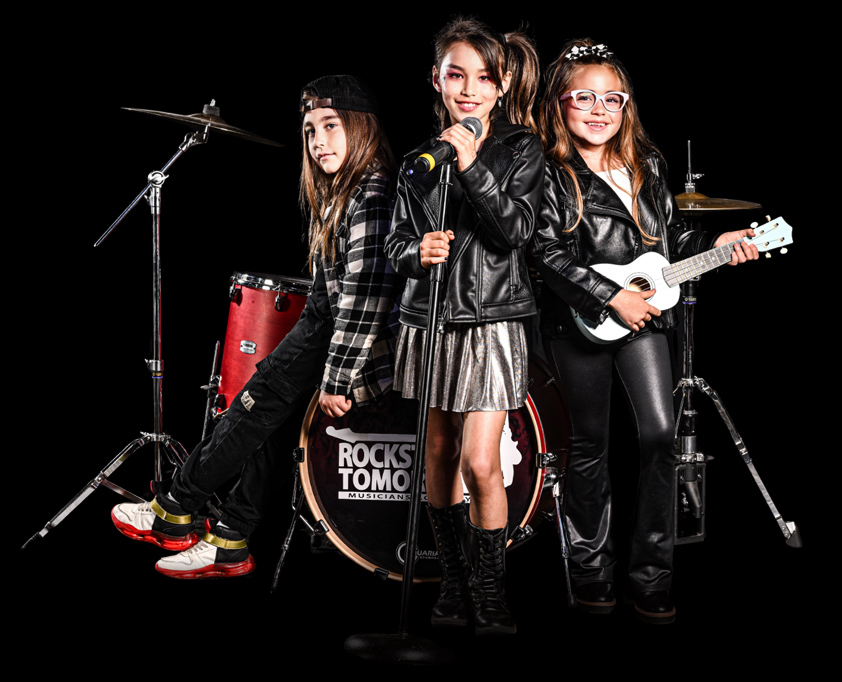 Three young musicians with drums, microphone, and ukulele performing in a Rockstars of Tomorrow music band program.
