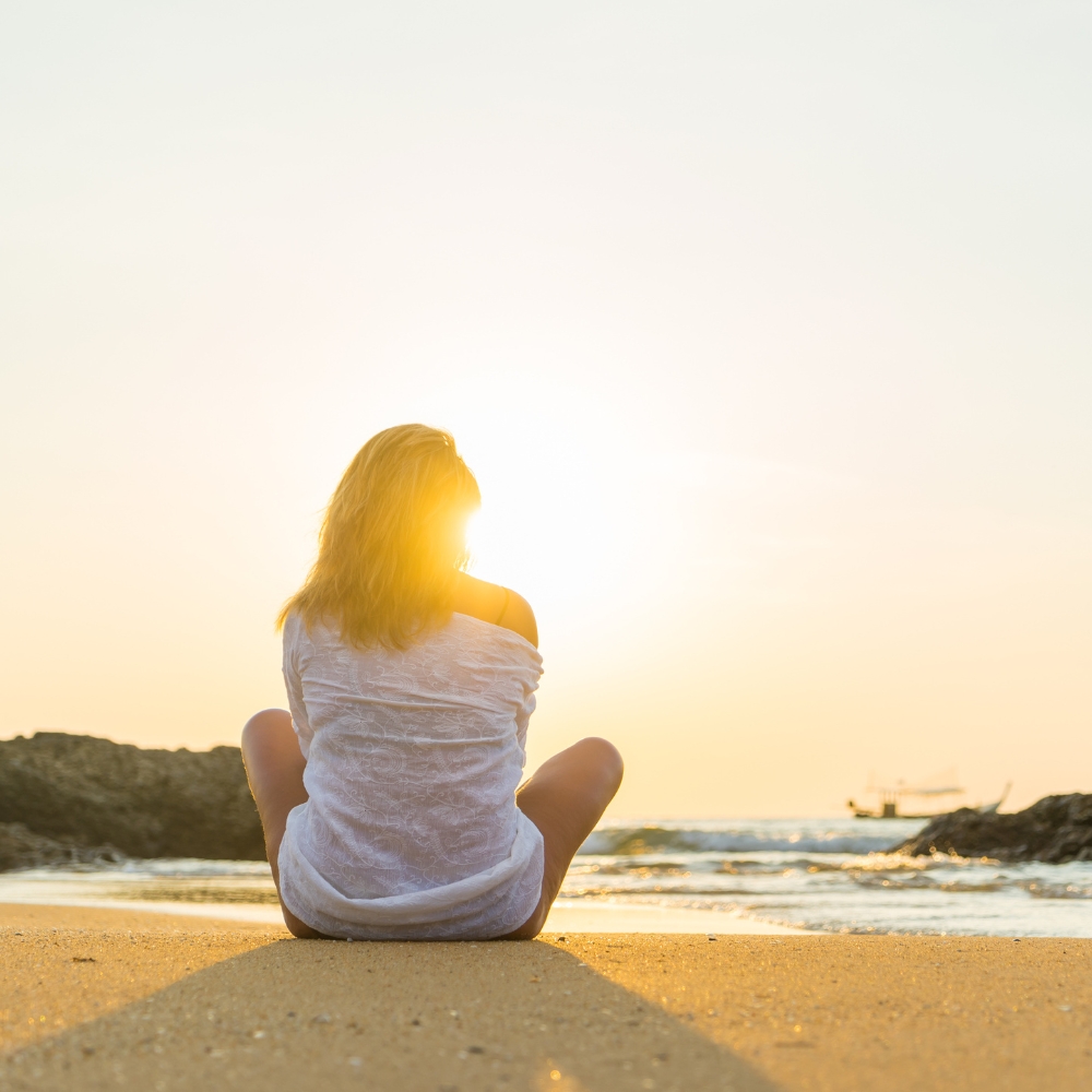 A woman sitting on the beach looking at the sun
