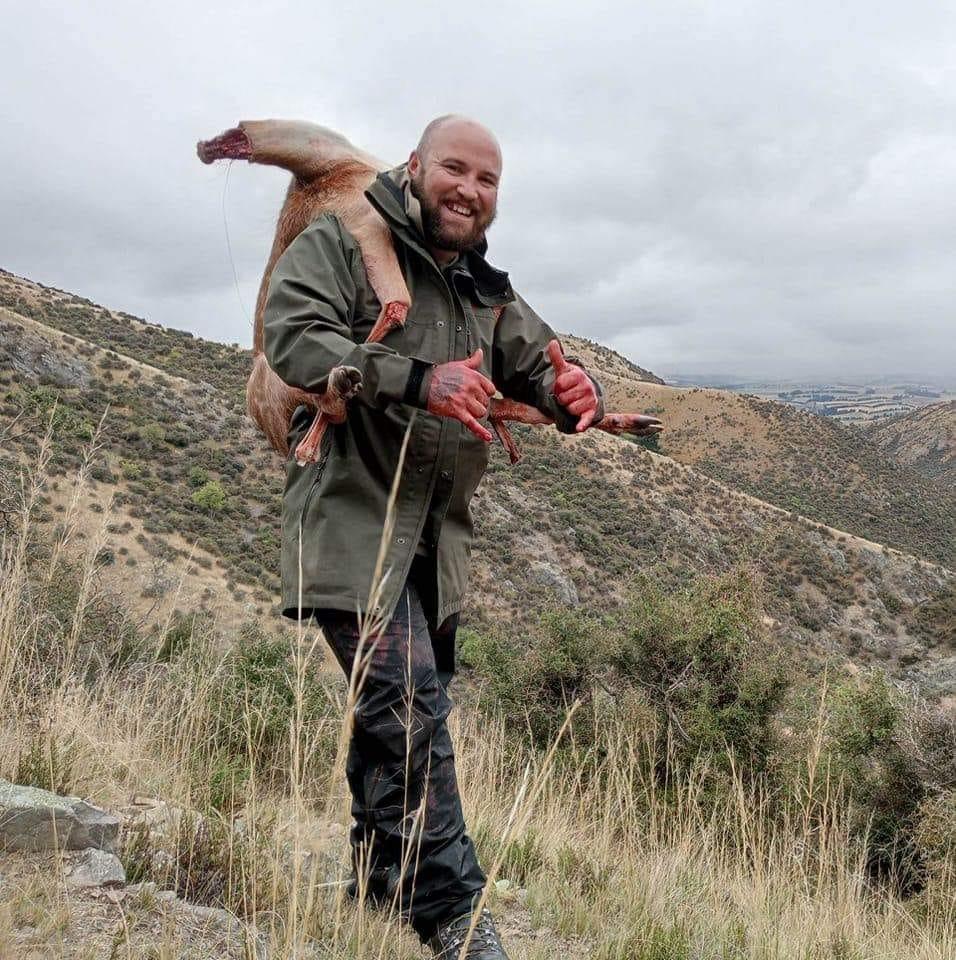 Pest control expert carrying game animal in Otago high country for humane removal services