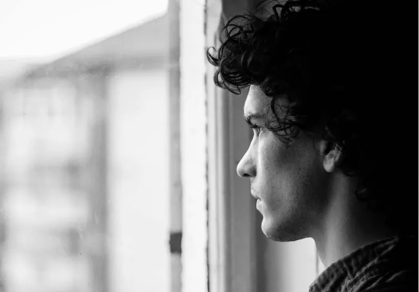 young man contemplating looking out a windw