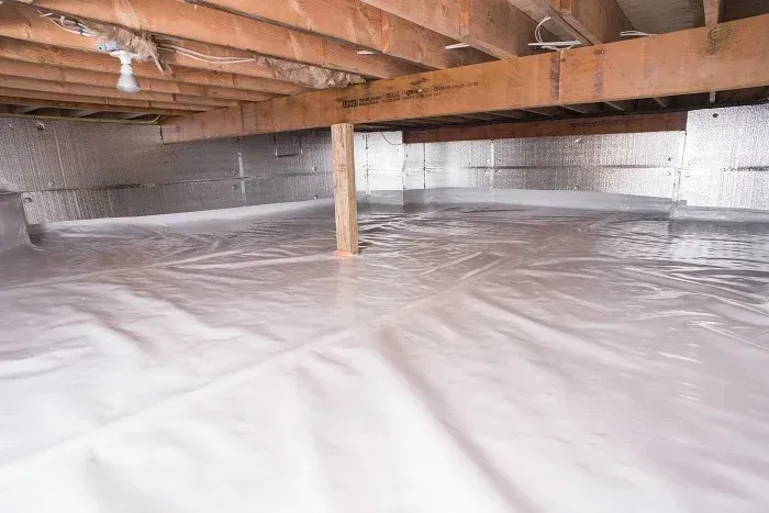 Moisture barrier installation under a house with plastic sheeting, showcasing pest control solutions for structural protection.
