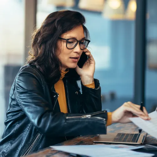 A field technician in high-visibility gear uses the JobVoice AI Assistant on a rugged tablet beside a white service van in an industrial yard, while an office manager monitors real-time updates on a desktop screen indoors. The scene is bright, modern, and dynamic, highlighting seamless technology integration in a trade environment.