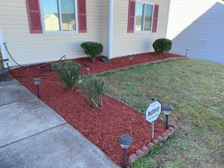 A tidy planter bed lined with red mulch and neatly trimmed green hedges in a residential yard.