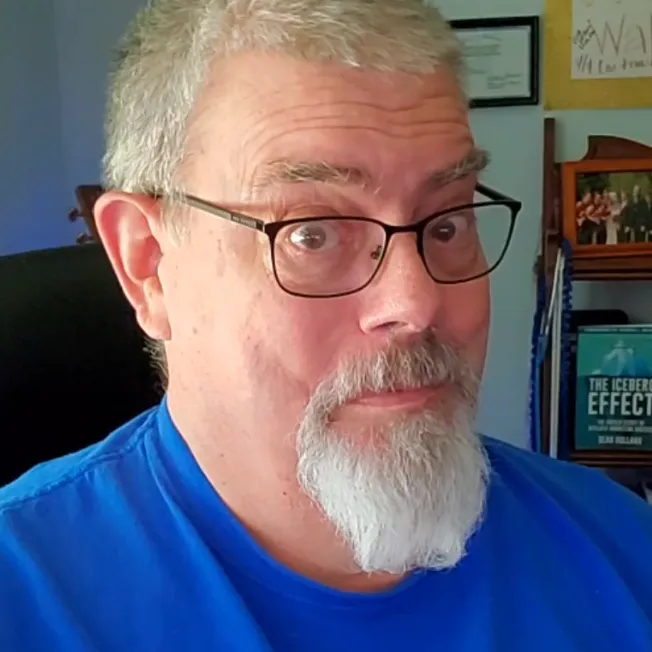 Mike Nelson, founder of MikeNelsonOnline.com, wearing glasses and a blue shirt with a thoughtful smile, sitting in his office — representing veteran insight, faith-based encouragement, and practical life wisdom.