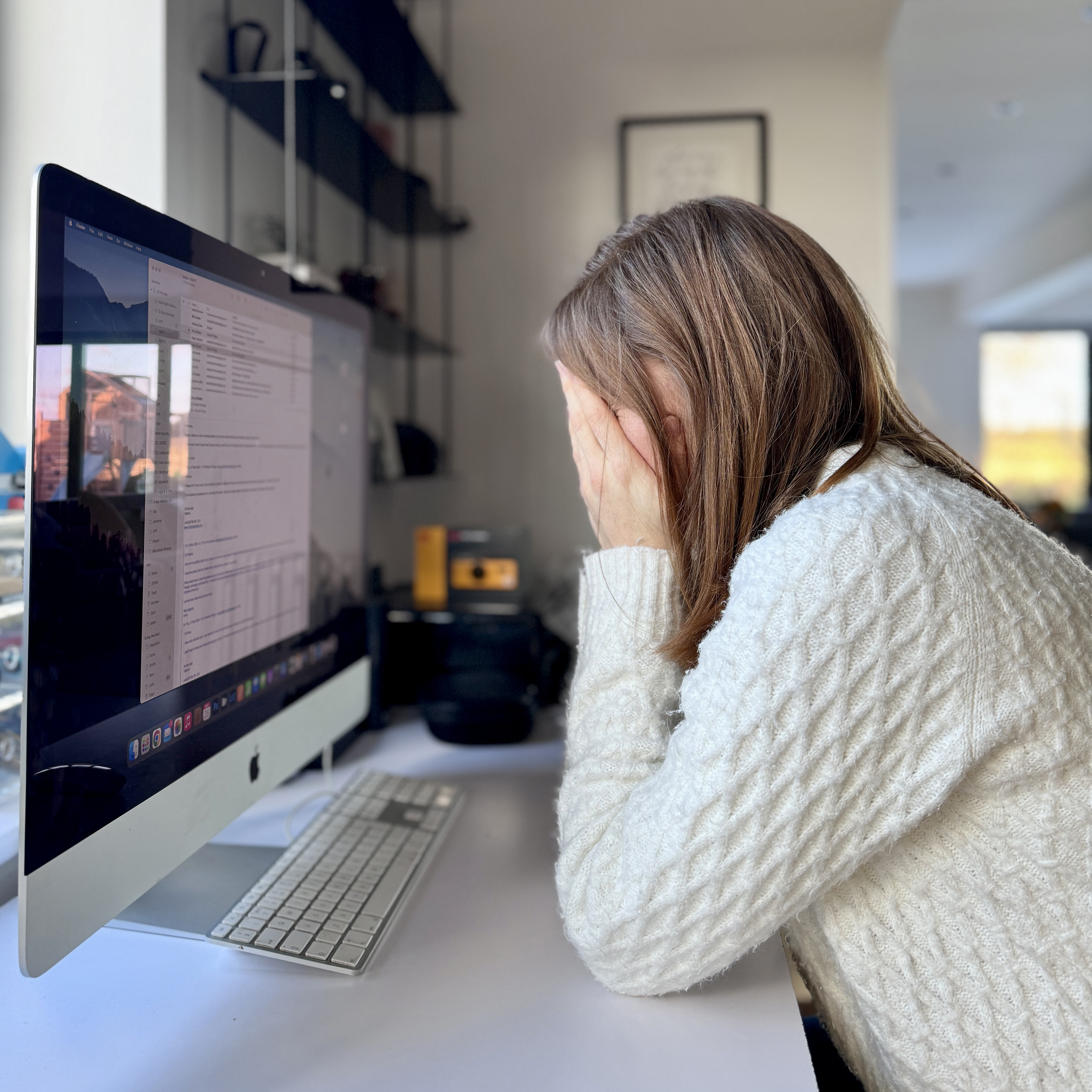 Burned out family portrait photographer sits with head in hands in front of the computer screen