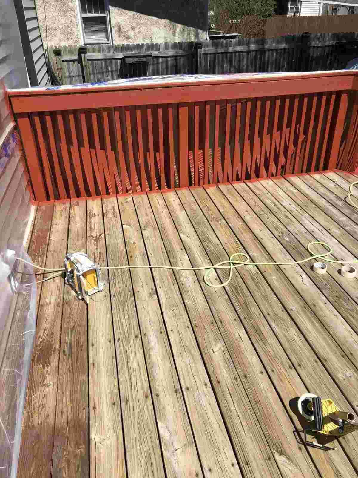 A partially renovated deck with a freshly painted orange railing and tools scattered on the wooden floor, showcasing a sunny outdoor setting.