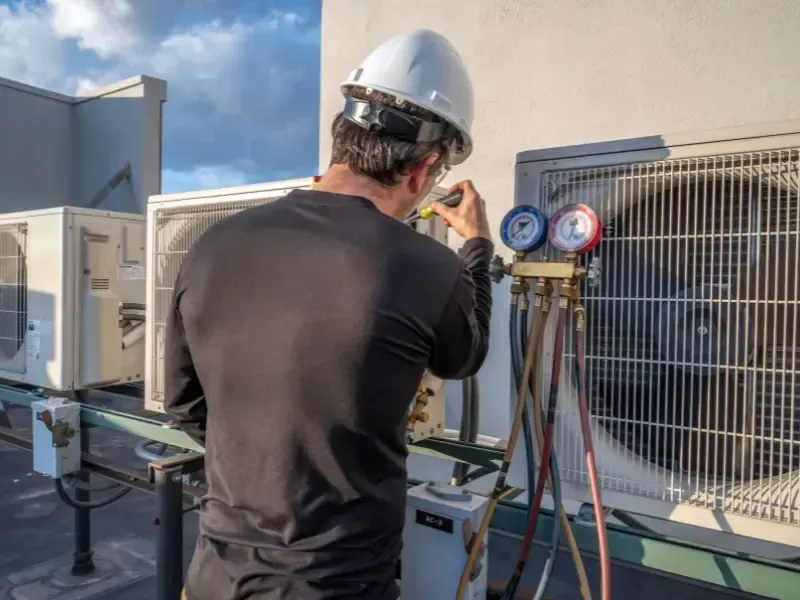 HVAC technician checking pressure gauges on a rooftop condenser unit.