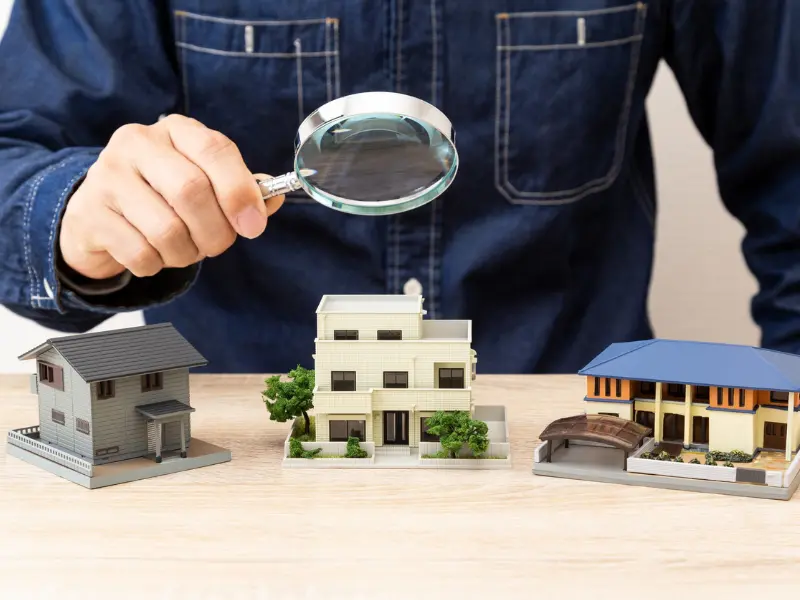 Inspector comparing home models with a magnifying glass, symbolizing residential property inspection and evaluation.