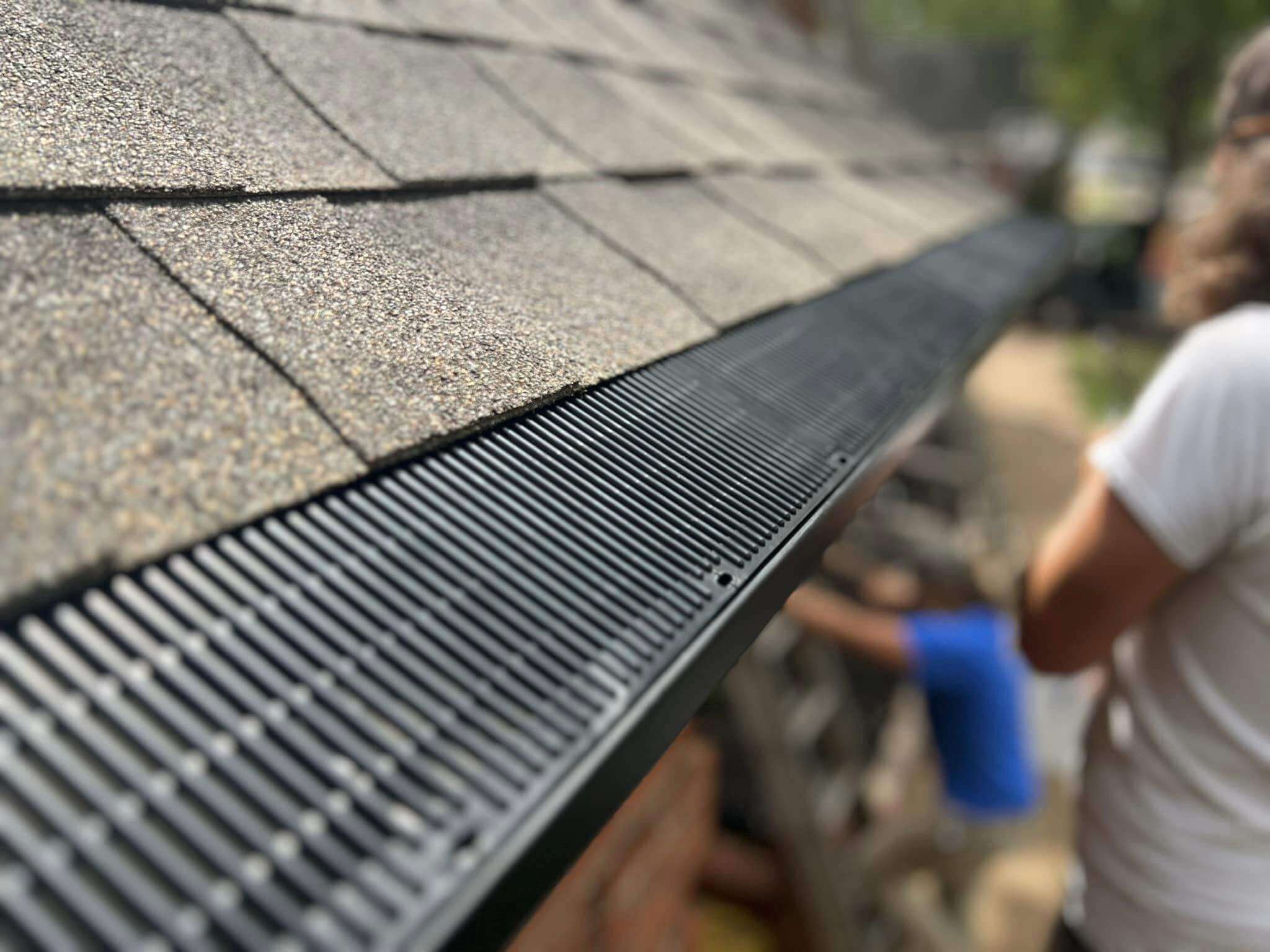 Close-up of a black micro-mesh gutter guard installed on a residential roof with asphalt shingles.