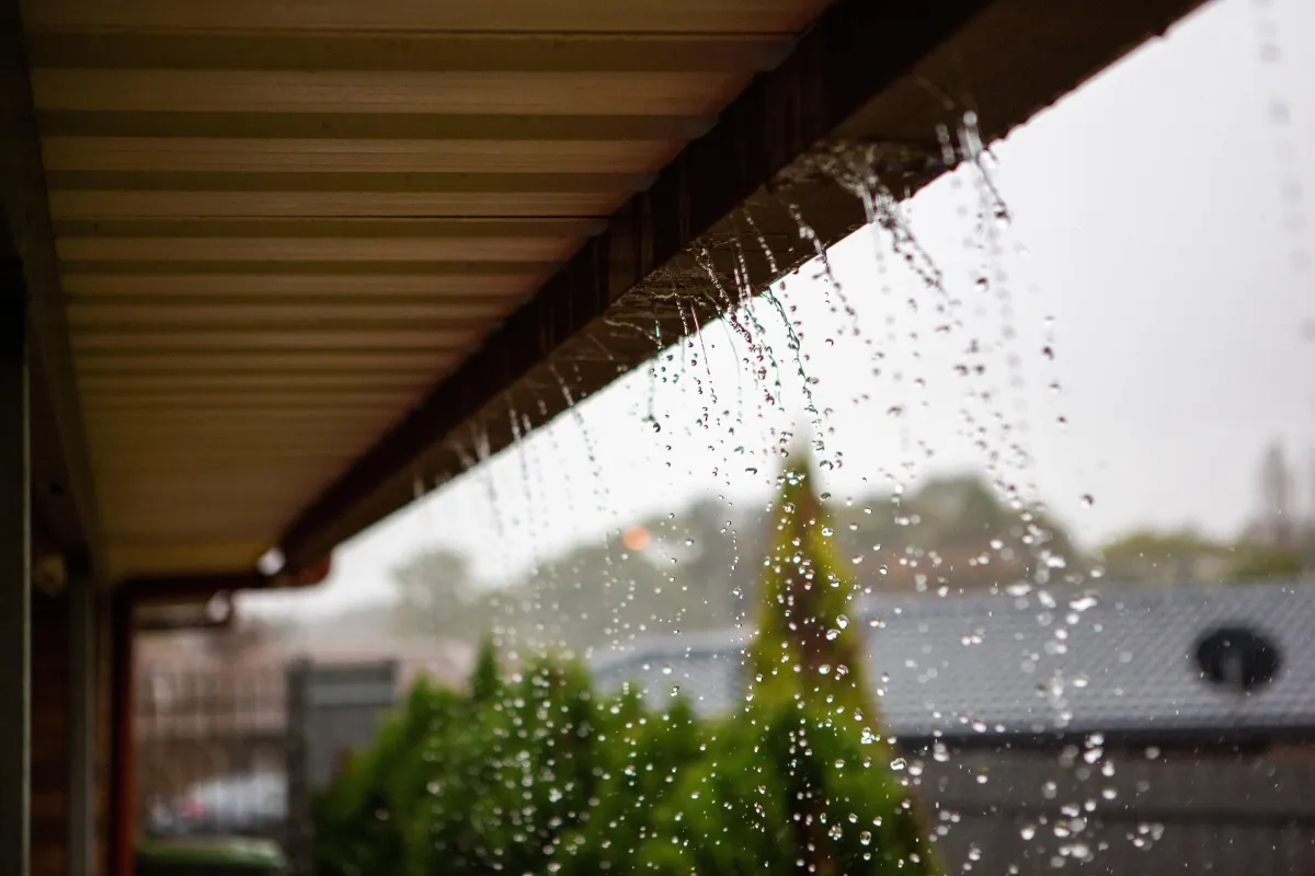 Heavy rain water overflowing and cascading over the edge of a residential house gutter line during a storm.