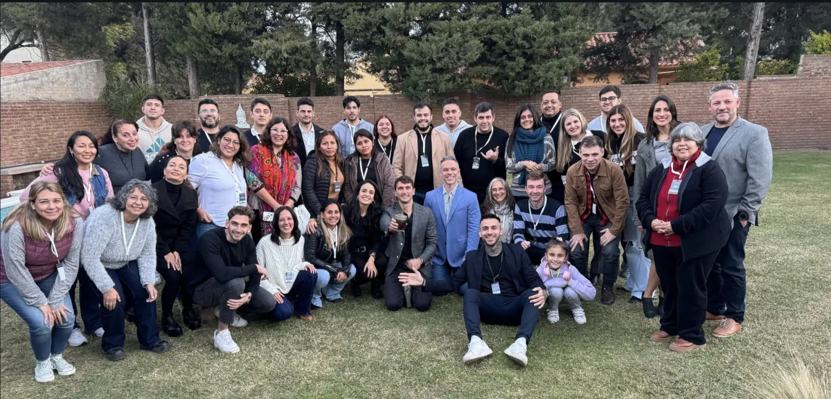 A group of coaches of various ages and backgrounds engaged in a lively roundtable discussion, with notepads and coffee cups, in a cozy, well-lit lounge. The setting emphasizes warmth, inclusivity, and active participation.