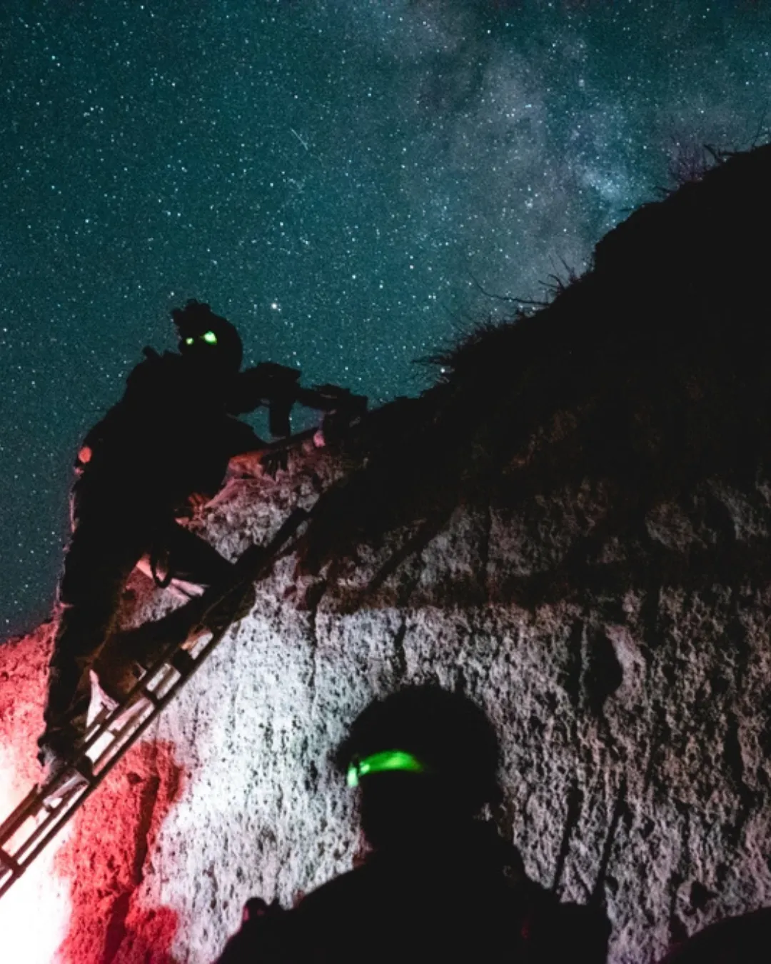 Two soldiers climb a rocky slope at night under a starry sky, wearing gear with glowing elements, creating an adventurous and mysterious tone.
