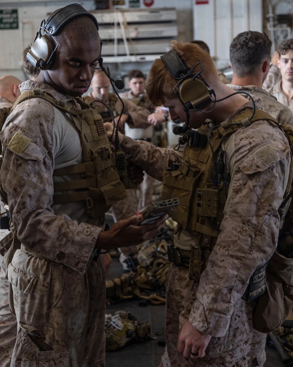 Several soldiers in camouflage gear prepare and adjust equipment inside a military transport aircraft, focusing intently on their tasks.