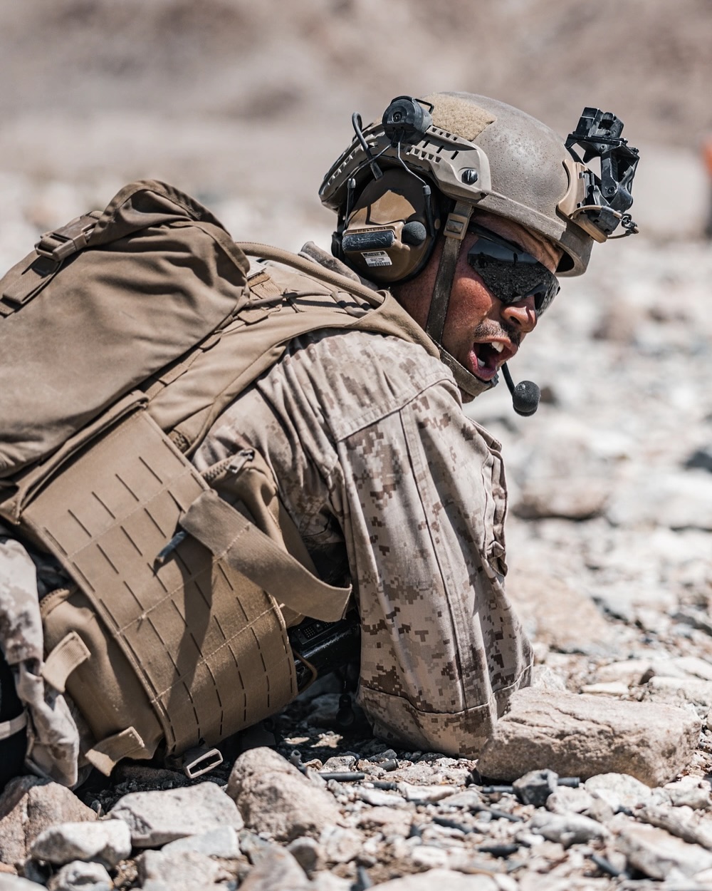 soldier in full combat gear laying on his stomach shouting over his shoulder