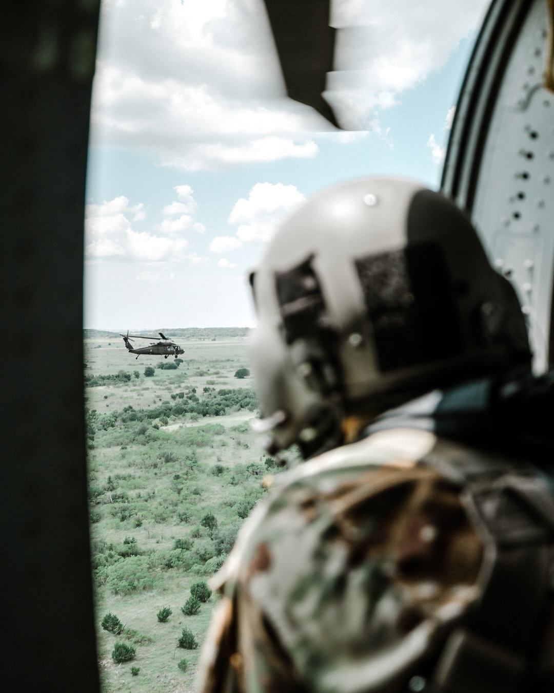 soldier looking out the side of a helicopter with the door open while it is flying through the air