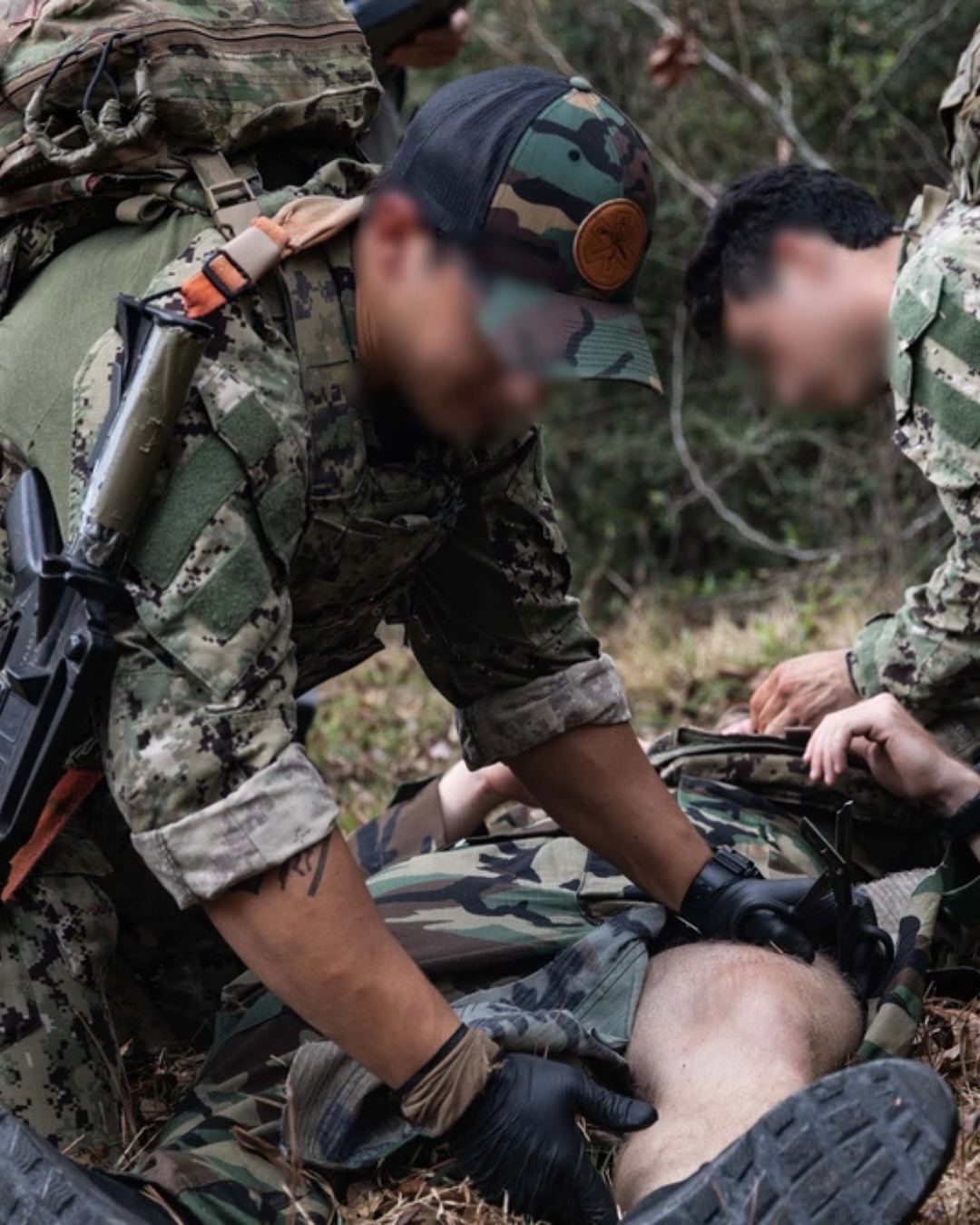 Soldiers in camouflage gear attend to a task in a forest setting, focusing intently. The scene suggests urgency and cooperation.