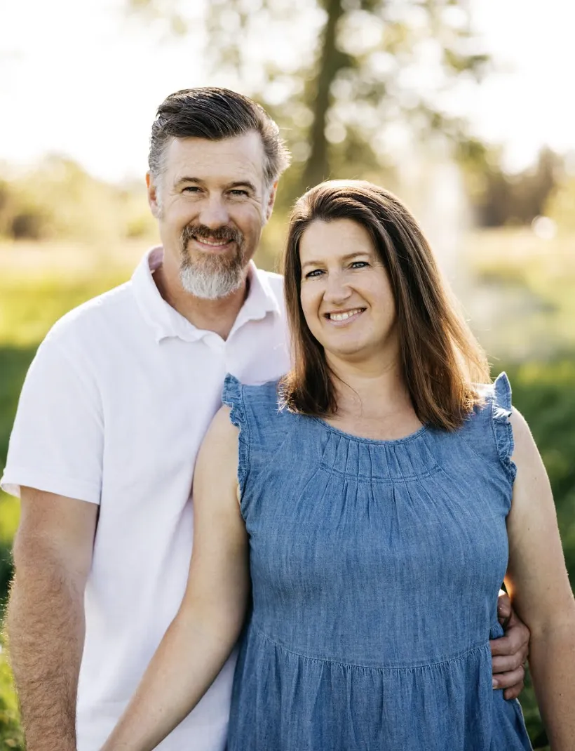 Smiling couple posing outdoors on a scenic wooded trail, dressed in smart casual attire, symbolizing partnership, success, and a balanced lifestyle.