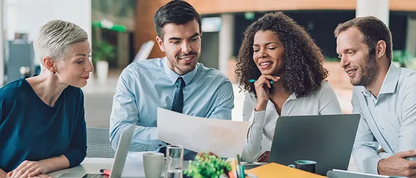 Group of professionals collaborating on a business strategy, reviewing documents and using technology, representing teamwork and training within the Impact Nation Training Portal.