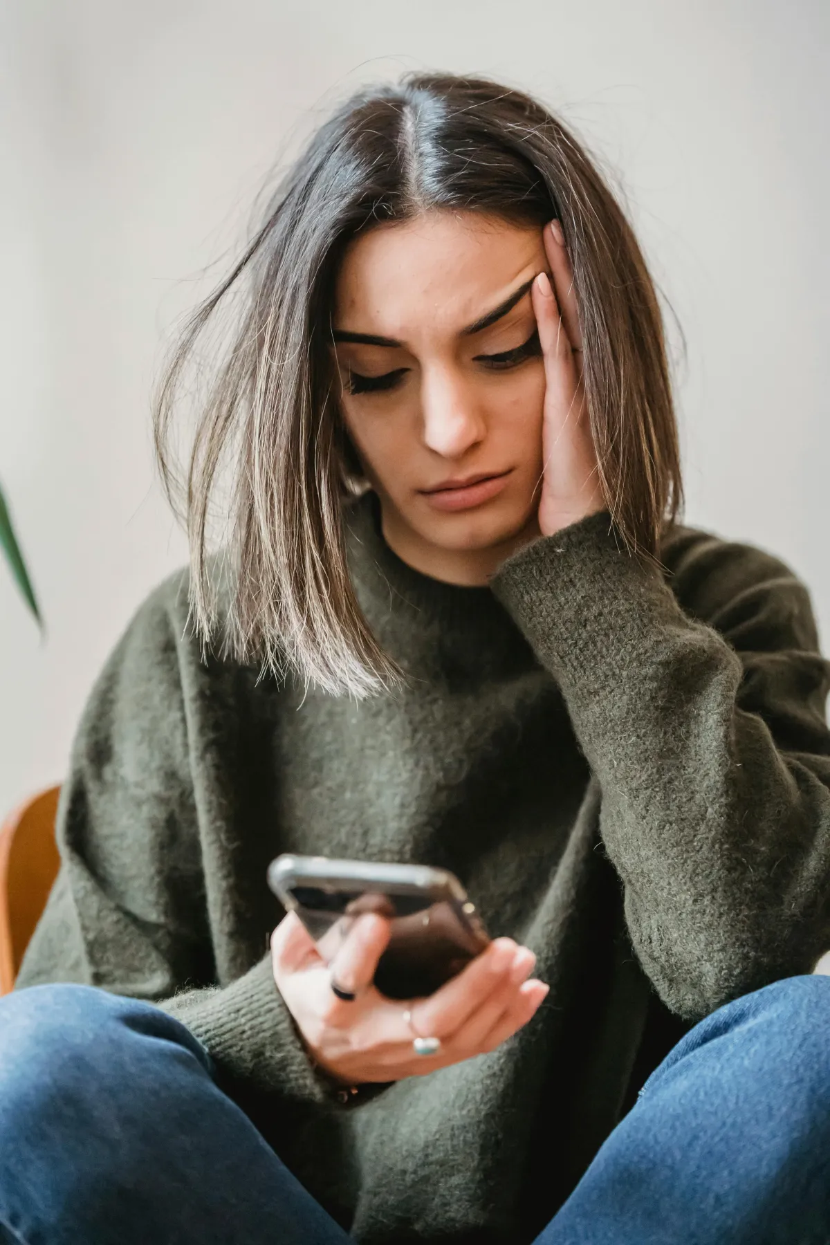 Woman with brown hair, a green sweater, and jeans reads a text from an irate client