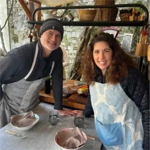 Two people smiling in a rustic kitchen setting, wearing aprons during a cooking class in Italy