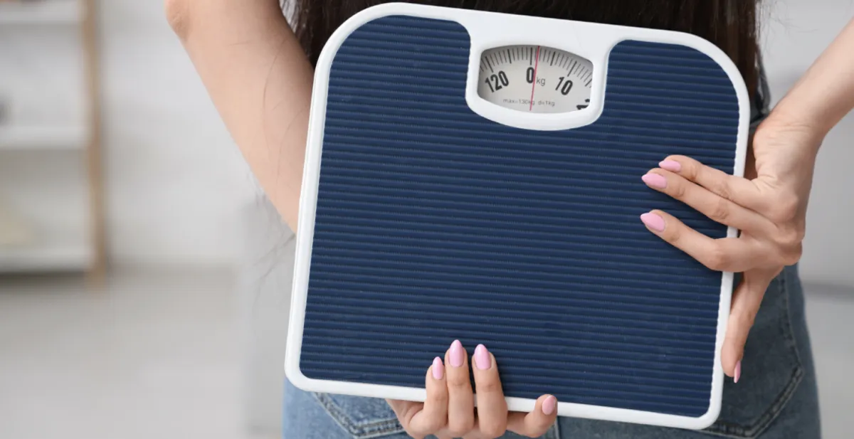 A person holding a bathroom scale, symbolizing frustration with weight loss progress, especially after age 40.