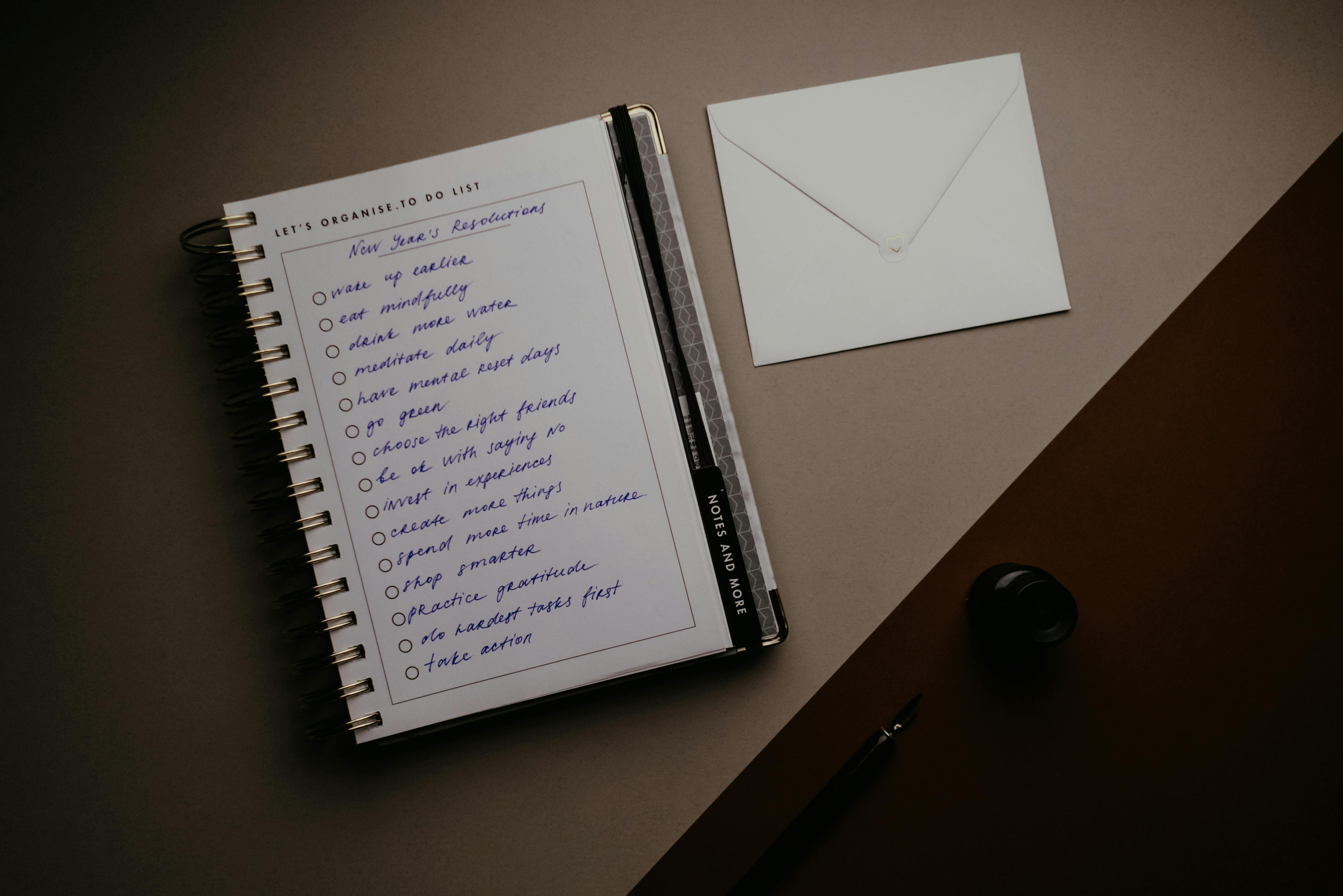 Hands on a laptop with a journal on a wooden table in warm morning light, conveying work and reflection.