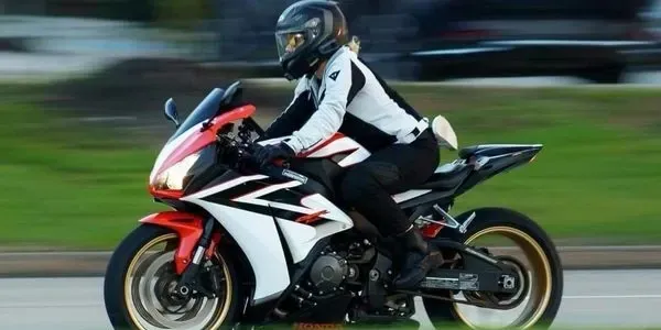 Sportbike rider wearing full protective gear riding on the street at speed, demonstrating proper body position and lane placement.