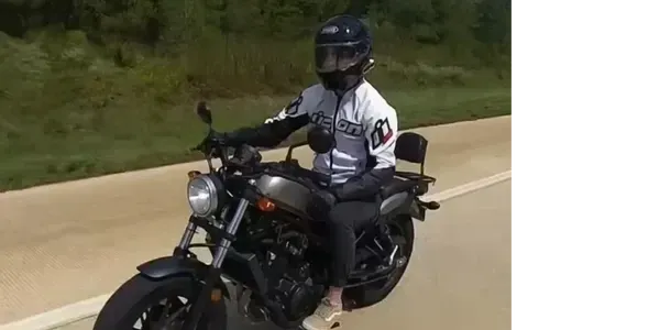 Motorcyclist riding a standard street bike in an upright position on a rural highway, wearing full protective gear and maintaining a relaxed, neutral posture.