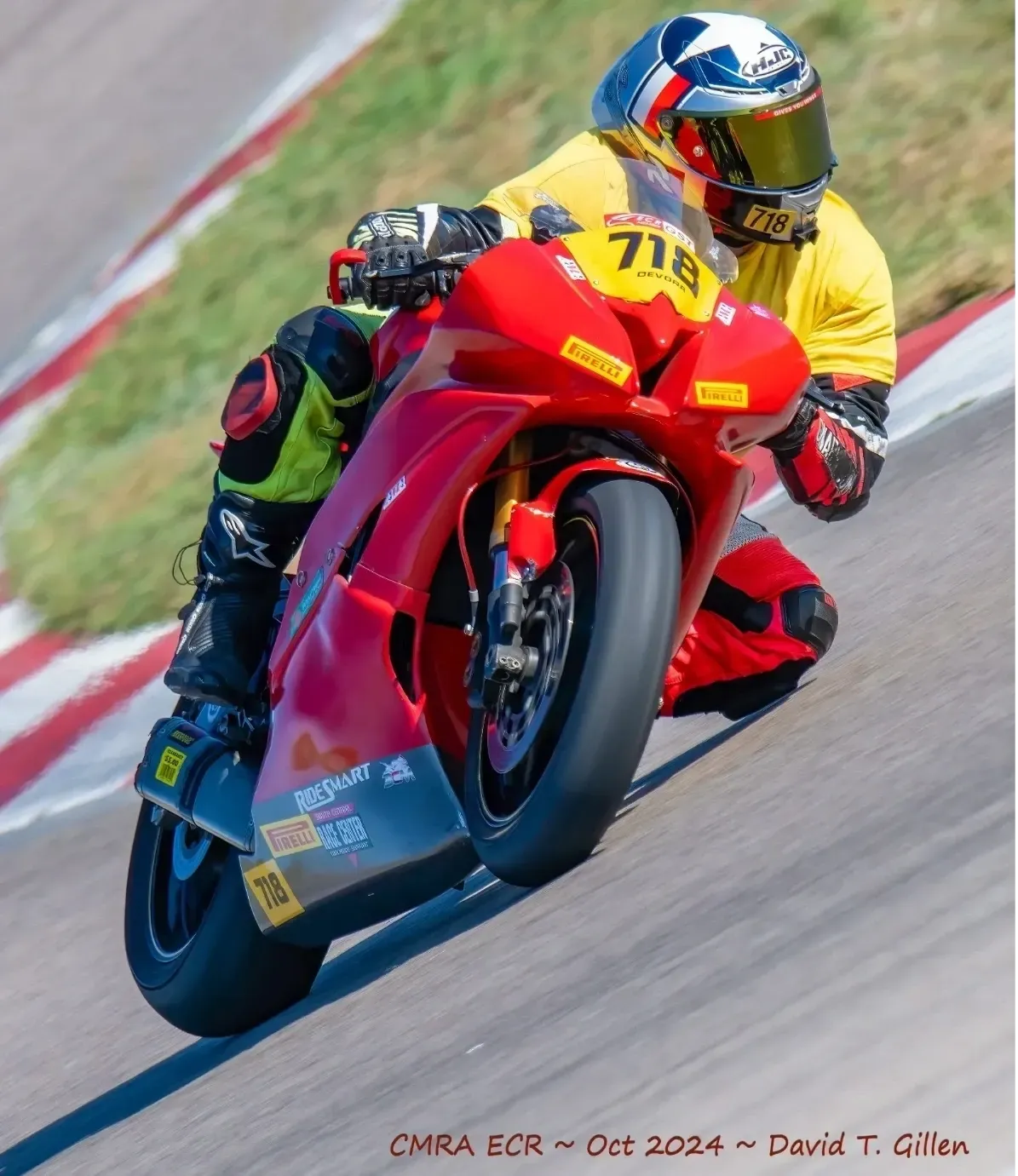Motorcycle road racer in a yellow jersey aggressively leaning a red sportbike through a paved track corner during a CMRA event, knee down and focused on the apex