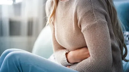 Person sitting with arms wrapped around their stomach, suggesting abdominal discomfort or pain.